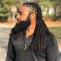 A man with long dreadlocks and beard standing on the side of a road.